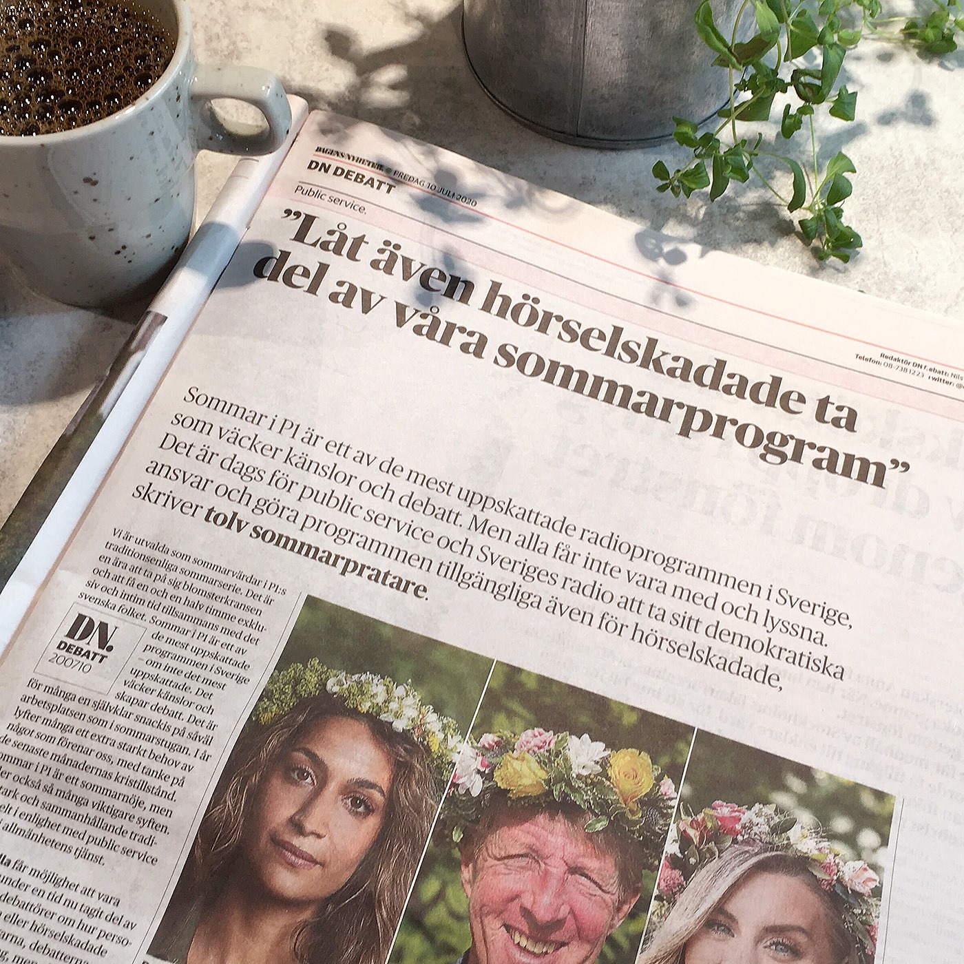 Foto, tidning på bord, kaffekopp, krukväxt. I tidningen rubriken "Låt även hörselskadade ta del av våra sommarprogram", tre porträttbilder av Rojda Sekersöz, Björn Natthiko Lindeblad och Therése Lindgren i blomsterkrans.