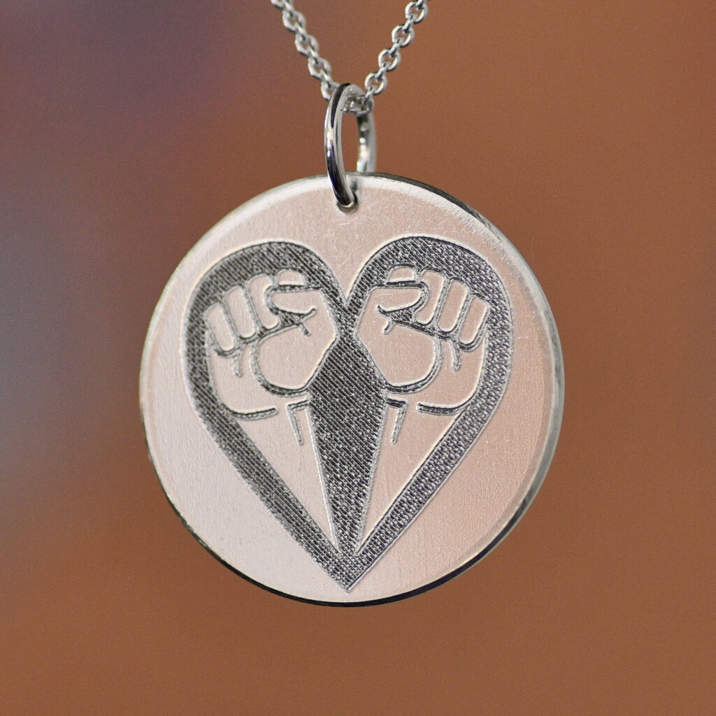 Rund silverplatta med utstandsad symbol av två knutna nävar som bildar ett hjärta